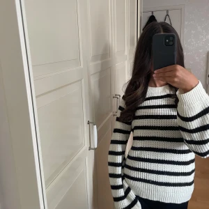 Randig stickad tröja i svart och vitt - Säljer en snygg stickad tröja med breda svarta och vita ränder. Tröjan har rund hals, ribbade muddar och långärmad passform. Perfekt för dig som gillar klassisk stil med en modern twist. Materialet är grovstickat och känns riktigt mjukt och skönt.