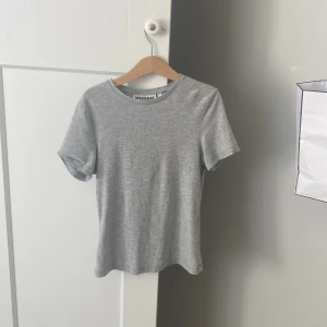 Grå t-shirt från Weekday XS - Snygg grå t-shirt från Weekday i storlek XS. Modellen är klassisk med rund hals och korta ärmar, perfekt för en clean och enkel look. Materialet är mjuk bomull som sitter skönt och har en slim passform. Passar dig som gillar stilrena basplagg.