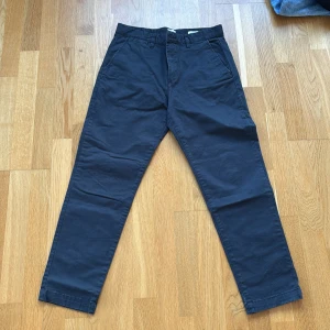 Mörkblå slim fit chinos från H&M - Snygga mörkblå chinos från H&M i slim fit-modell med stretch. Byxorna har klassisk knapp och dragkedja framtill, bälteshällor och fickor både fram och bak med knappstängning. Materialet är mjuk bomull med lite elastan för extra komfort.