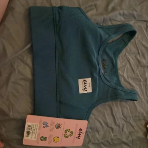 Blå ribbad linnetopp från Eivy - Säljer en blå ribbad sportBH från Eivy i modellen Rider Rib Sports Bra, färgen heter Deep Sea. Toppen har breda axelband och en sportig, tight passform med elastisk kant nedtill. Perfekt för träning och aktiva dagar, tillverkad i stretchigt syntetmaterial. Aldrig använd 