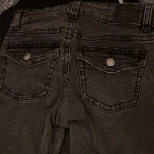 Mörkgrå bootcut jeans från Gina tricot  - Snygga mörkgrå bootcut jeans från gina tricot med låg midja och coola ficklock bak med silverfärgade knappar. Jeansen har klassisk femficksdesign, bälteshällor och dragkedja fram. Kan ta bättre bilder i ljuset om de önskas💗