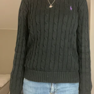  stickad tröja från Polo Ralph Lauren - Svart kabelstickad tröja från Polo Ralph Lauren med lila broderad logga på bröstet. Rund halsringning och långa ärmar. Tröjan har ribbade muddar vid ärmslut och nederkant, vilket ger en snygg och klassisk look. Sparsamt andvänd och i gått skick! Priset går att diskuteras vi snabb affär.