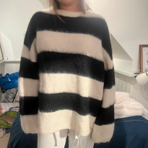 Svartvit randig stickad tröja - Mysig oversized stickad tröja med breda svarta och vita ränder. Tröjan har rund hals och långa ärmar, och är fluffig i materialet vilket ger en cool och avslappnad vibe. Perfekt för dig som gillar statement-plagg med enkel design.