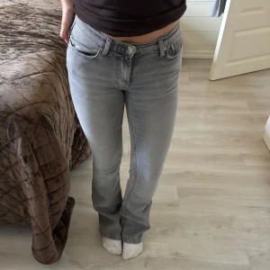Grå bootcut jeans med låg midja från Gina Tricot - Snygga grå jeans med bootcut passform och låg midj från Gina Tricot. Jeansen har klassisk femficksdesign, bälteshällor och dragkedja med knapp framtill. Materialet är mjukt jeans och färgen är ljusgrå med lite tvättad look. Perfekta för dig som gillar retrovibbar och stilren look. Helt oanvända💕💕