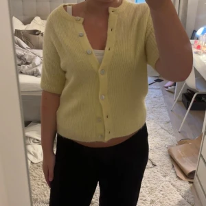 Gul stickad kofta från Gina Tricot - Superfin ljusgul stickad kofta från Gina Tricot med kort ärm och rund hals. Koftan har ribbad struktur och knäpps med silvriga knappar framtill. Perfekt att slänga över ett linne för en chill look.