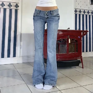 Bootcut jeans från American Eagle - Snygga bootcut jeans från American Eagle i ljusblå denim. Lågmidjade med klassiska fem fickor och coola slitningar på bakfickorna. Jeansen har en avslappnad passform över låren och utsvängda ben, perfekt för en trendig 00-talslook.