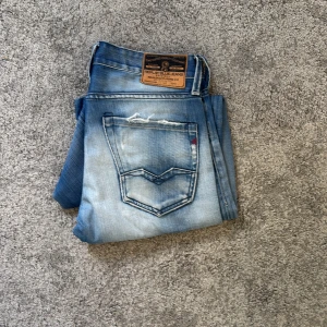 Replay  ljusblå slitna jeans - Säljer ett par Replay  jeans i ljusblå tvätt med slitningar och hål på knäna. Klassisk femficksmodell med snygga detaljer på bakfickan och läderpatch i midjan. Jeansen har en slim passform och är tillverkade i mjukt denimtyg.