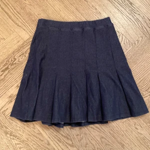 Mörkblå veckad denim/jeanskjol från Zara - Snygg mörkblå plisserad mjukt jeans tyg från Zara i klassisk modell. Kjolen har en kort längd och är tillverkad i jeansmaterial som ger en cool och tidlös vibe. Perfekt att matcha med sneakers eller boots för en trendig look.