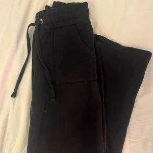 Svarta mjukisbyxor med snörning - Svarta mjukisbyxor med elastisk midja och snörning framtill. Byxorna har två fickor fram och två bakfickor, raka ben och är gjorda i mjukt bomullsmaterial. Perfekta för chill dagar eller när du vill vara extra bekväm.