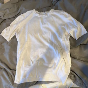 Vit ribbad t-shirt från Zara - Vit t-shirt från Zara i storlek L. T-shirten har korta ärmar, ribbade muddar vid ärmslut och nederkant samt en klassisk rund halsringning. Materialet känns mjukt och har en lätt glansig finish, perfekt för en clean och stilren look.