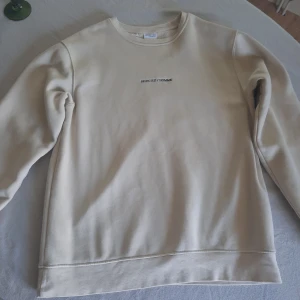 Beige sweatshirt från Selected Homme - Snygg beige sweatshirt från Selected Homme med broderad logga på bröstet. Tröjan har rund halsringning och är tillverkad i mjuk bomullsmix med fleeceinsida. Perfekt för en chill och stilren look.