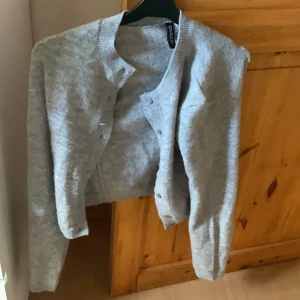 Grå kofta från H&M Divided - Mysig grå kofta från H&M Divided med rund halsringning och knappar framtill. Långärmad och ribbade muddar vid ärmslut och nederkant. Perfekt att slänga över en t-shirt eller linne för en chill look. Storlek xxs men stämmer inte eftersom den sitter som storlek S säljer för att den tyvärr är för stor