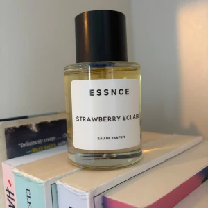 ESSNCE Strawberry Eclair parfym - En stilren parfymflaska från ESSNCE med doften Strawberry Eclair. Flaskan är cylindrisk i genomskinligt glas med svart lock och vit etikett med svart text. Innehållet är ljusgult och parfymen är en Eau de Parfum. Endast testad 
