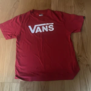 Röd Vans t-shirt med logga XL - Röd t-shirt från Vans i klassisk modell med stor vit Vans-logga på bröstet. Skön passform och tillverkad i 100% bomull. Perfekt för dig som gillar en lungn, chill look.