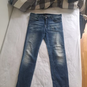Blå jeans från J.Lindeberg - Snygga blå jeans från J.Lindeberg med klassisk femficksdesign och coola slitningar framtill och baktill. Jeansen har raka ben och normal passform, tillverkade i mjukt denimtyg. Perfekta för en avslappnad och trendig look.