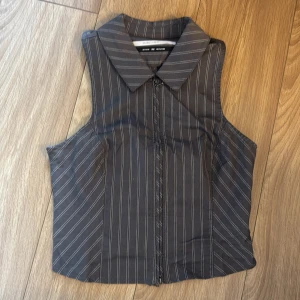 Randig väst från Silence + Noise - Snygg svart väst med tunna vita ränder från Silence + Noise. Modellen har klassisk krage, dragkedja framtill och figurnära passform. Perfekt att styla över en skjorta eller t-shirt för en cool look.