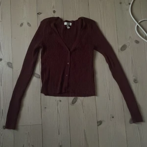 Vinröd ribbad kofta/tröja från H&M - Vinröd ribbad kofta/tröja från H&M med v-ringning och knappar framtill. Modellen är figurnära med långa ärmar och tillverkad i ett stretchigt material. Bra i passform.  