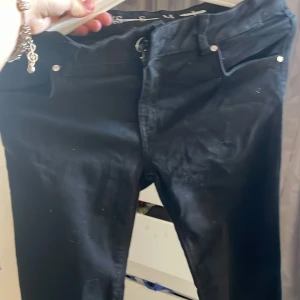 Svarta jeansbyxor med raka ben - Säljer ett par svarta skinni jeans med klassisk femficksdesign och raka ben. Byxorna har normal passform och är tillverkade i bomullsmix med en snygg matt finish. Perfekta för dig som gillar en clean och enkel look.