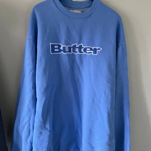 Blå sweatshirt från Butter, stl L - Säljer en oversized ljusblå sweatshirt från Butter med tryckt logga framtill. Tröjan har rund hals, långa ärmar och är gjord i mjuk bomullsmix. Perfekt för en chill och avslappnad stil.