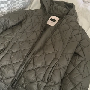 Quiltad grå jacka från Part Two - Snygg quiltad jacka från Part Two i en mörkgrå/grön nyans. Jackan har huva, dragkedja framtill och ett stilrent rutmönster. Perfekt för dig som gillar en clean look. Passar till det mesta och är lätt att matcha. pris går att diskutera 