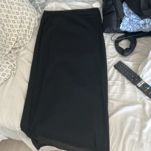 Svart långkjol i mjukt tyg - Enkel och stilren svart långkjol med rak passform. Kjolen är i ett mjukt och följsamt material, perfekt för dig som gillar minimalistisk stil. Passar till sneakers eller boots för en clean look.