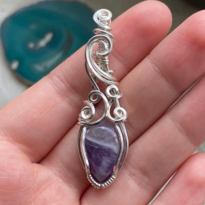 Handgjord silverberlock med ametist - Unik berlock med en lila ametist infattad i snirklig silvertråd. Stenen har vackra naturliga mönster och infattningen är handgjord med coola detaljer och swirl-design. Perfekt för dig som gillar boho eller magiska vibes.