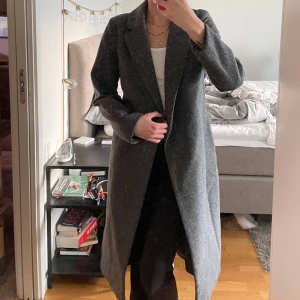 Mörkgrå kappa med bälte - Säljer en lång, mörkgrå kappa som använts väl fickorna har därmed gått sönder men borde gå att sy ihop! Därav billiga priset för den fungerar fortfarande att bära😇