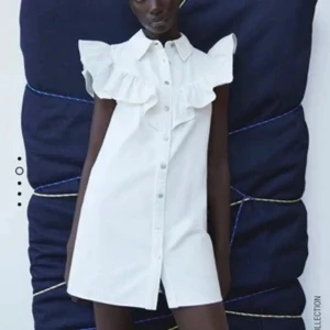 Vit klänning - Superfin vit kort skjortklänning med volangdetaljer över axlarna och bröstet. Klänningen har knappar hela vägen framtill och klassisk skjortkrage. Perfekt för dig som gillar en söt och trendig look.                          Pris kan diskuteras❣️