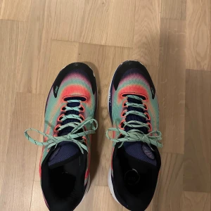Färgglada Under Armour sneakers - Säljer ett par riktigt färgstarka Under Armour sneakers med coolt gradientmönster i grönt, rosa, lila och svart. Skorna har snörning, vit sula och ventilerande meshmaterial. Perfekta för dig som vill sticka ut på gymmet eller i vardagen.