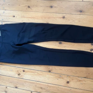 Svarta tights från Stronger - Svarta tights från Stronger med diskreta reflexprickar på benet och bred midja. Snygga sömmar och stretchigt material som sitter tight och bekvämt. Perfekta för träning eller chill dagar.
