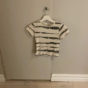 Randig croppad topp från KappAhl - Säljer en croppad topp från KappAhl i vitt med svarta ränder. T-shirten har korta ärmar, rund hals och är tillverkad i ribbad bomull. Perfekt för dig som gillar en chill och trendig stil.