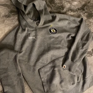 Grå BAPE x Puma hoodie med logga - Säljer en grå hoodie från BAPE x Puma i storlek small med BAPE.F.C-logga på bröstet och klassisk Puma-logga. Tröjan har huva, magficka och muddar. 