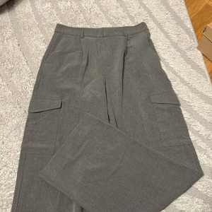 Grå cargobyxor med raka ben - Snygga grå cargobyxor med raka ben och stora fickor på sidorna. Byxorna har bälteshällor och en stilren look som passar till många outfits. Materialet känns mjukt och har en lätt kostymkänsla. Perfekta för dig som gillar en clean och modern stil.