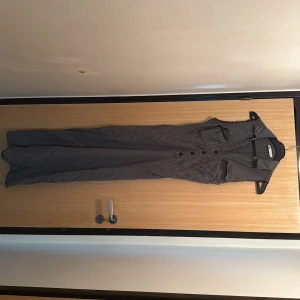 Grå långklänning med knappar - Snygg grå långklänning från Zara med ärmlös design, krage och knappar framtill. Klänningen har två bröstfickor och råa kanter vid ärmhålen för en cool look. Perfekt för dig som gillar minimalistisk stil.