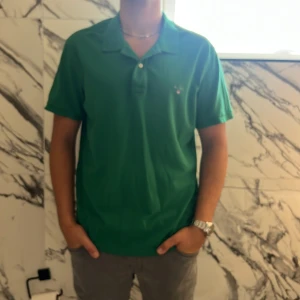 Grön pikétröja från GANT 2XL - Snygg grön pikétröja från GANT i storlek 2XL. Klassisk modell med krage, korta ärmar och knappar framtill. Broderad GANT-logga på bröstet. Tillverkad i mjuk bomull som känns skön mot huden.