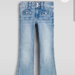 Snygga Ljusblå bootcut jeans med fickdetaljer - Low waist ljusblå jeans med bootcut passform och coola fickor framtill med lock och knappar. Jeansen har dubbla knappar i midjan och klassisk femficksdesign. Perfekta för dig som gillar retrovibbar och vill ha en avslappnad men trendig look. Storlek 164 men passar mig som är 160 och har xs/s