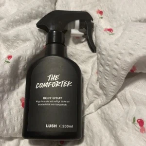 Lush The Comforter Body Spray 200ml - The Comforter Body Spray från Lush i en svart plastflaska med spraymunstycke. Doften är söt och bärig med inslag av svartvinbär och bergamott. Flaskan rymmer 200 ml och har en modern, stilren design. Pris kan diskuteras