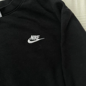 Svart Nike sweatshirt i bomull - Svart sweatshirt från Nike med klassisk broderad logga i vitt på bröstet. Tröjan har rund halsringning och är tillverkad i mjuk bomull, perfekt för en chill och sportig look. Långärmad modell som funkar året runt.