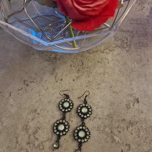 Svarta glittriga statement-örhängen - Långa svarta örhängen med tre runda sektioner, dekorerade med glittrande stenar i cirklar. Perfekta för att sticka ut och ge en cool touch till din look. Hängande modell med krokar för enkel användning.