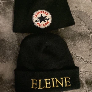 Svarta mössor Converse & Eleine - Två svarta mössor: en från Converse med klassisk rund patch med stjärna och röd text, och en med guldbroderad 'ELEINE' framtill. Båda är ribbstickade och har uppvikt kant. 