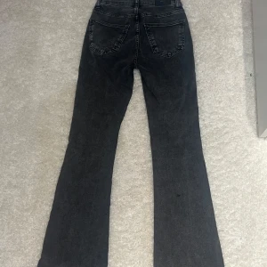 Svarta bootcut jeans med hög midja - Säljer ett par svarta bootcut jeans med hög midja. Jeansen har klassisk femficksdesign, snygg tvättad look och sitter tajt upptill med utsvängda ben. Innerbenslängd: ca 80cm             Midjemått rakt över: 35cm