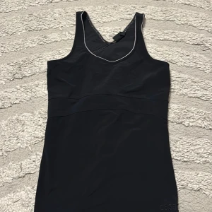 Svart sportig kortklänning - En svart, ärmlös och sportig kortklänning med rundad halsringning och diskret kontrastsöm. Perfekt för dig som gillar en enkel och stilren look. Materialet känns stretchigt och följsamt.