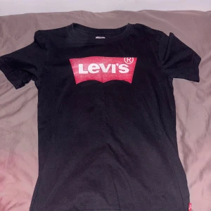 2-pack Levi's t-shirts med logga - Två snygga t-shirts från Levi's med klassisk logga på bröstet. En svart med röd/vit logga och en vit med blå/röd logga. Båda är i ca 170 och är i helt okej skick hör av er vid frågor.