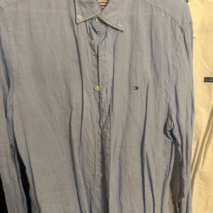 Ljusblå linneskjorta Tommy Hilfiger - Snygg ljusblå skjorta från Tommy Hilfiger i linne med klassisk krage och knappar framtill. Liten broderad logga på bröstet ger en clean look. Perfekt till jeans eller chinos för en avslappnad stil.