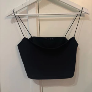 Svart croppad linnetopp från NLY One - Snygg svart croppad linnetopp från NLY One med tunna axelband och stilren design. Enkel att matcha med både jeans och kjol.