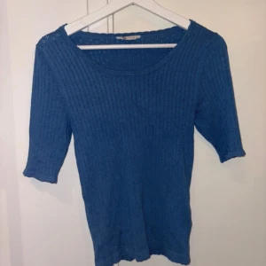 Blå stickad topp med trekvartsärm - Snygg blå stickad topp med trekvartsärm och rund halsringning. Ribbad struktur som ger en stilren och enkel look. Perfekt att matcha med jeans eller kjol för en avslappnad stil.