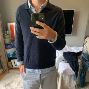 Mörkblå kashmirtröja från Soft Goat - Säljer en mörkblå långärmad tröja från Soft Goat i 100% kashmir. Tröjan har klassisk krage och v-ringning, perfekt för en clean och stilren look. Passformen är normal och materialet är supermjukt och lyxigt. Den har ett litet hål i armhålan.