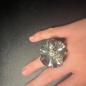Stor silverring med blomma och pärla - Unik och statement silverfärgad ring i form av en stor blomma med en vit pärla i mitten. Aldrig använd och är i fint skick. (Köpte från litet smyckesföretag, så vet ej om de är bra kvalitet) Hör av dig om det är någoty! 