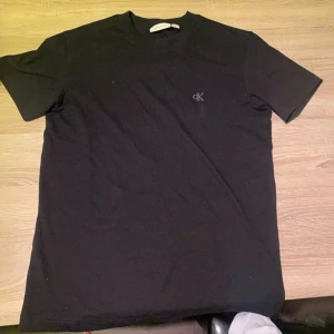 Svart t-shirt från Calvin Klein Jeans - Svart t-shirt från Calvin Klein Jeans med diskret CK-logga på bröstet. Klassisk rund halsringning och korta ärmar. Tillverkad i mjuk bomull för en skön känsla. Perfekt basic-plagg med clean look.