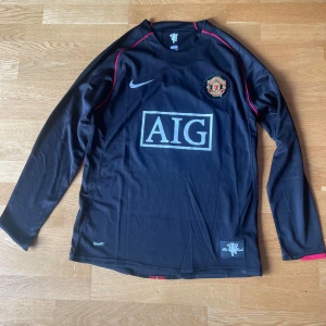 Manchester United Ronaldo 7 långärmad tröja - Säljer en svart långärmad Manchester United fotbollströja från Nike med Ronaldo 7 på ryggen. Tröjan har röda detaljer, klubbmärke på bröstet och AIG som sponsor. Tillverkad i lätt och ventilerande NikeFIT-material, perfekt för dig som älskar fotboll och United.